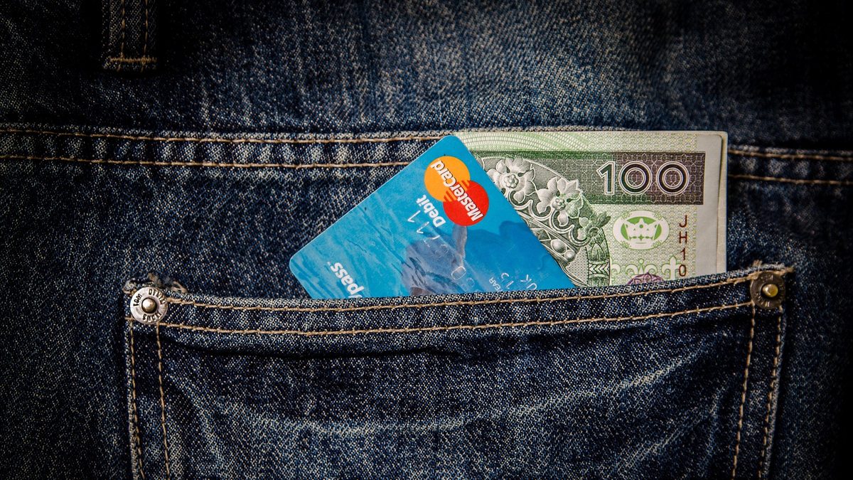 A debit card and a banknote tucked into the back pocket of a pair of jeans