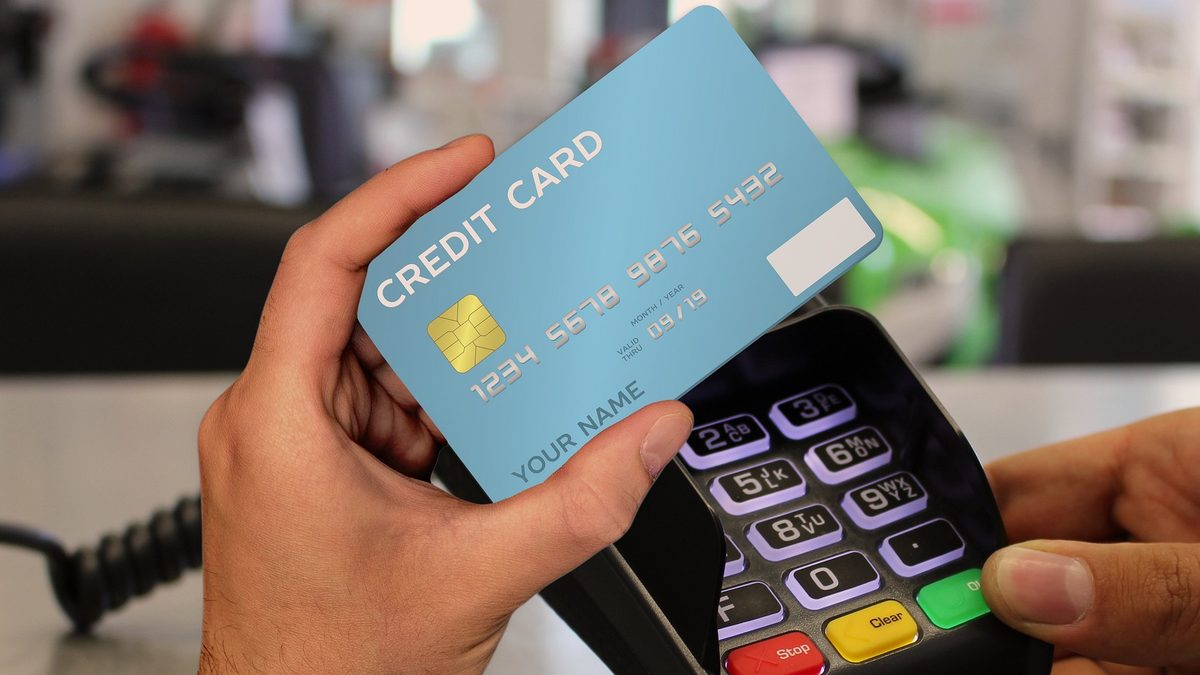 A hand holding a credit card up to a card payment terminal