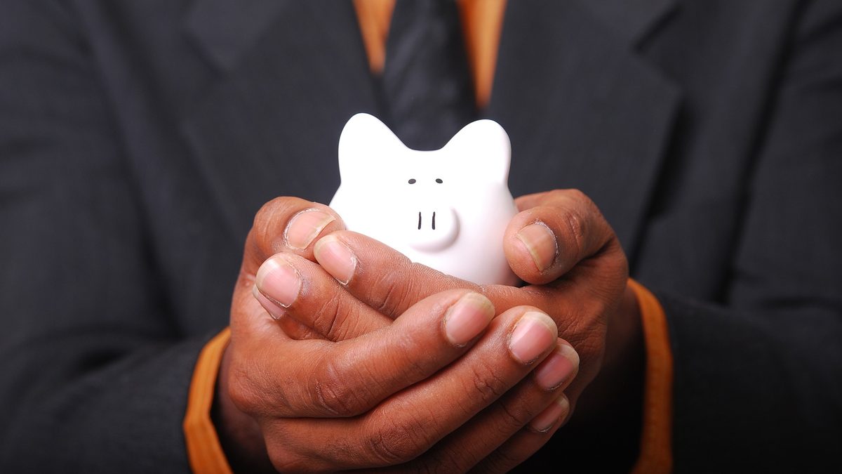 A person in a suit holding a small white piggy bank in cupped hands