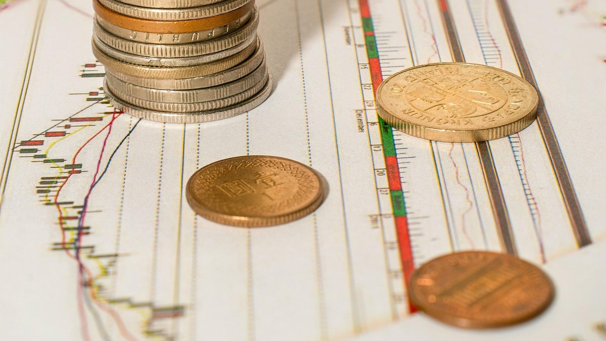 A stack of coins and loose coins resting on printed financial charts