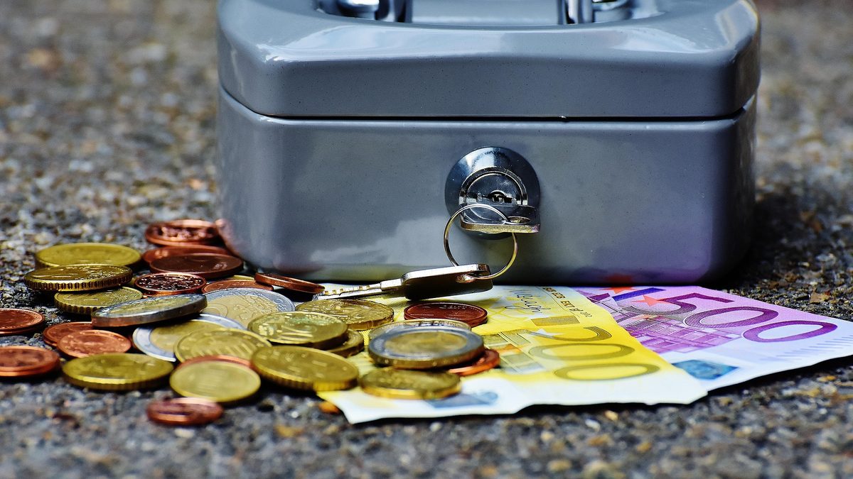 A small locked gray cash box with a key, surrounded by euro coins and a banknote